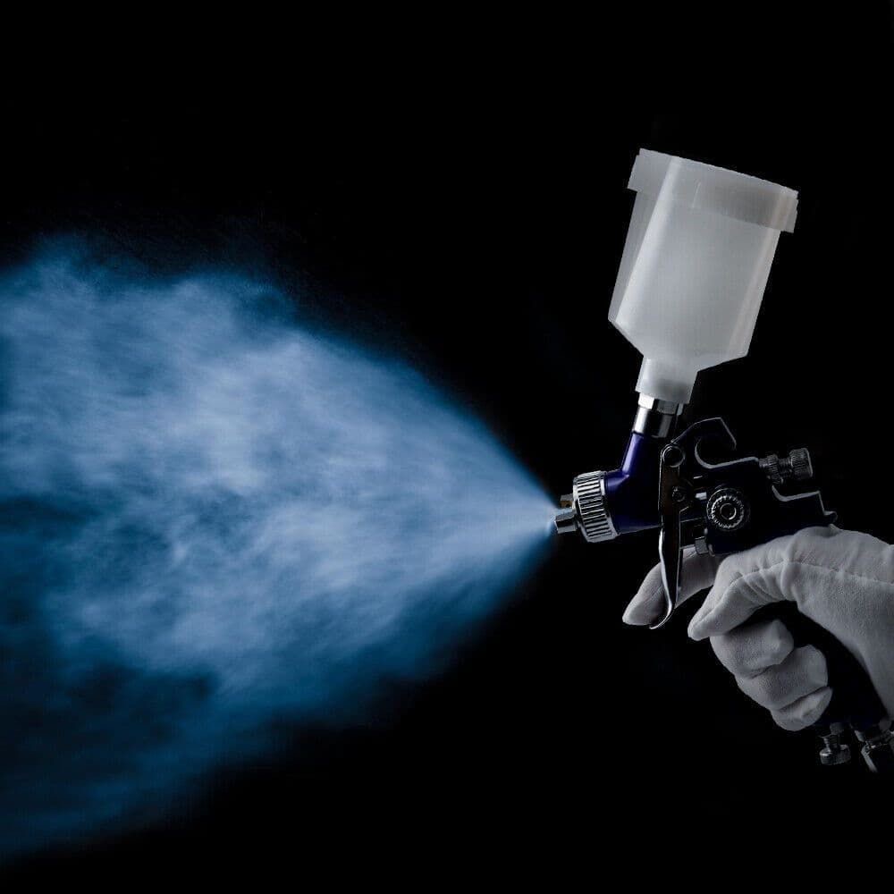 Detailer in white gloves spraying a fine mist from a professional spray gun